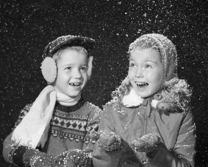 1950S Boy Girl In Winter Dress Hats Gloves Ear Muffs Scarf Smiling Happy Fake Snow Flakes Falling Studio Shot