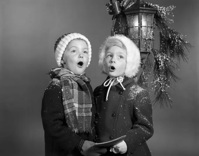 1960S Boy And Girl Singing Christmas Carol Together Under Snowy Outdoor Porch Light