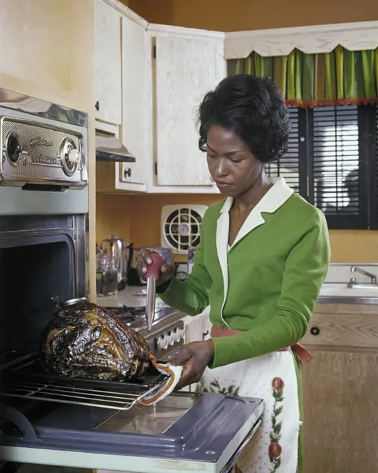 1980s AFRICAN-AMERICAN WOMAN HOUSEWIFE BASTING A TURKEY IN ELECTRIC WALL OVEN 