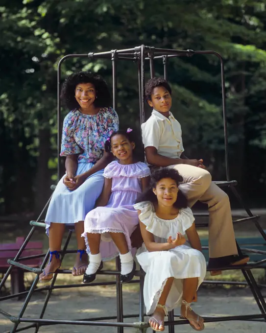 1980s FOUR AFRICAN-AMERICAN KIDS BOY AND THREE GIRLS BROTHER AND SISTERS SITTING ON PLAYGROUND CLIMBING GYM LOOKING AT CAMERA