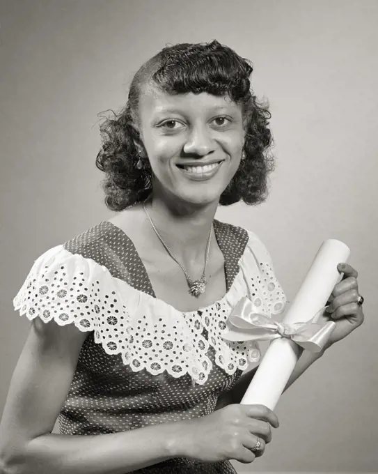 1950s AFRICAN-AMERICAN WOMAN HOLDING COLLEGE DIPLOMA LOOKING AT CAMERA SMILING PROUDLY WEARING DOTTED SWISS DRESS LACY COLLAR
