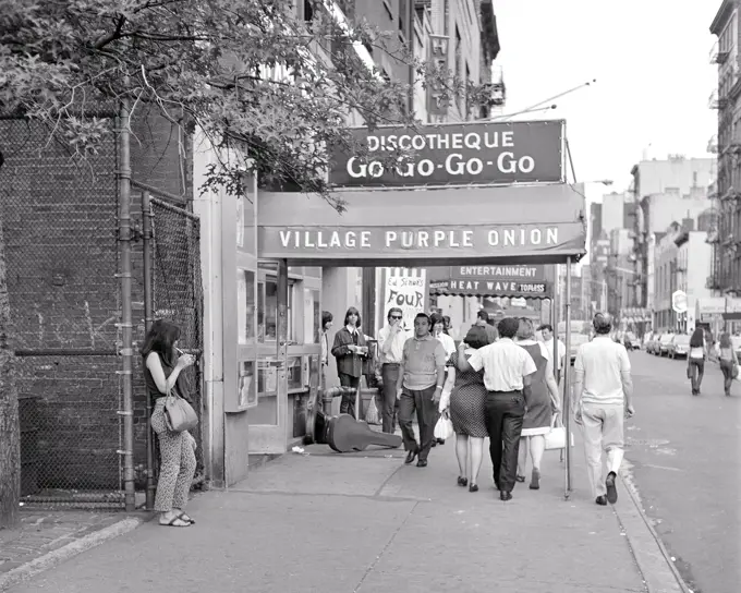 1960s GREENWICH VILLAGE CITY STREET SCENE GROUP OF YOUNG ADULTS WALKING ALONG PAST THE PURPLE ONION A FAMOUS GO-GO BAR NYC USA