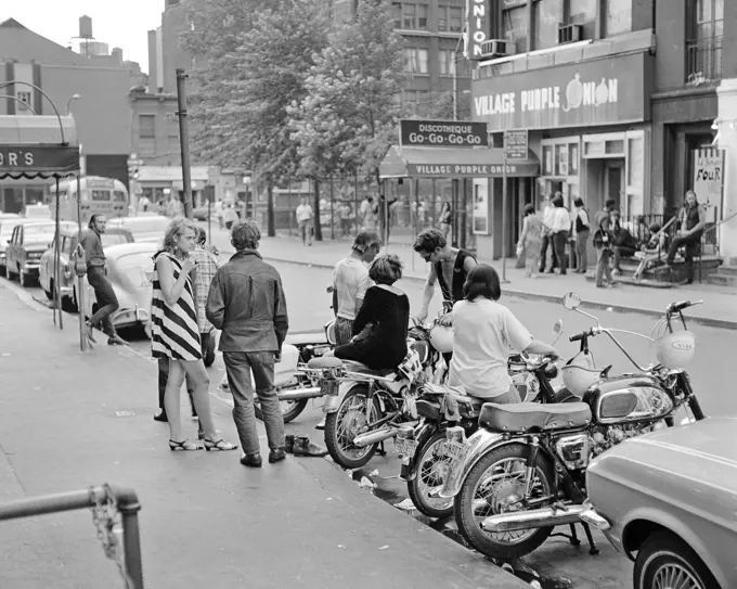 1960s GREENWICH VILLAGE STREET SCENE GROUP OF YOUNG ADULTS BY MOTOR BIKES ACROSS STREET FROM THE PURPLE ONION A FAMOUS GO-GO BAR