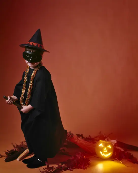 1960s GIRL DRESSED HALLOWEEN COSTUME A WITCH WITH MASK RIDING A BROOM PUMPKIN JACK-O-LANTERN BEHIND HER 