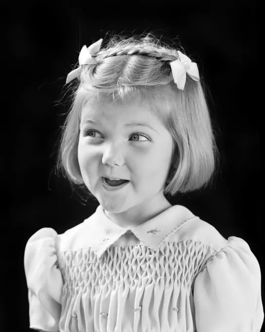 1940s SMILING CUTE BLOND GIRL LOOKING OFF TO SIDE WITH MISCHIEF IN EYES BOWS AND BRAID IN HAIR AND SMOCKING ON DRESS 