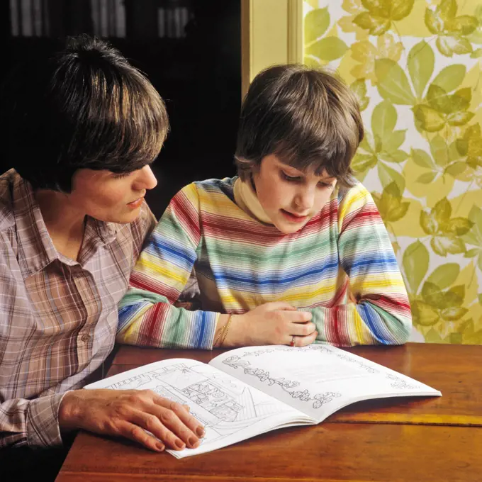 1980s MOTHER HELPING HER DAUGHTER WITH READING HOME WORK 