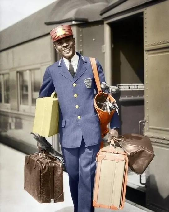 1930s SMILING AFRICAN-AMERICAN MAN RED CAP PORTER CARRYING LUGGAGE IN TRAIN STATION 