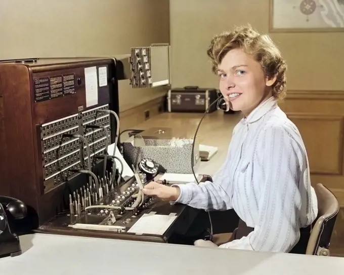 1950s SMILING WOMAN OFFICE TELEPHONE SWITCHBOARD OPERATOR RECEPTIONIST LOOKING AT CAMERA
