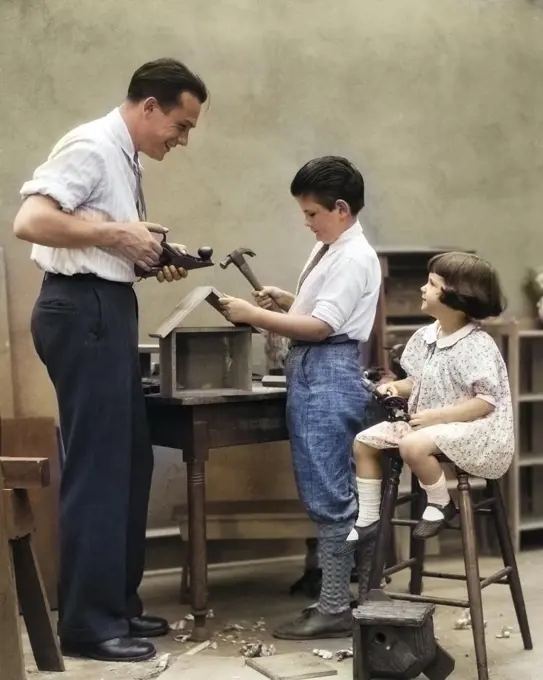 1920s FAMILY FATHER CARPENTER TEACHING SON AND DAUGHTER TO BUILD A BIRDHOUSE WITH WOODWORKING TOOLSI