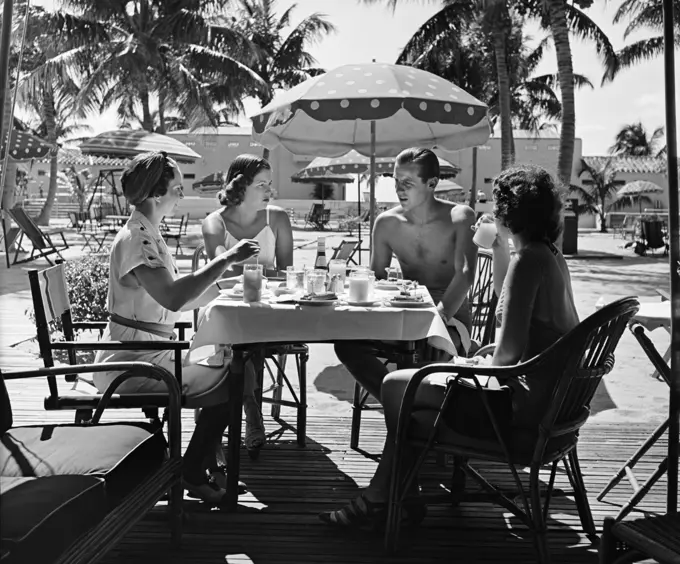 1950S Three Women And One Man Sitting At Tropical Pool Side Table Talking