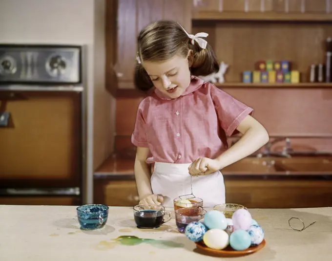 1960s SMILING GIRL WEARING PINK BLOUSE DYEING EASTER EGGS IN KITCHEN