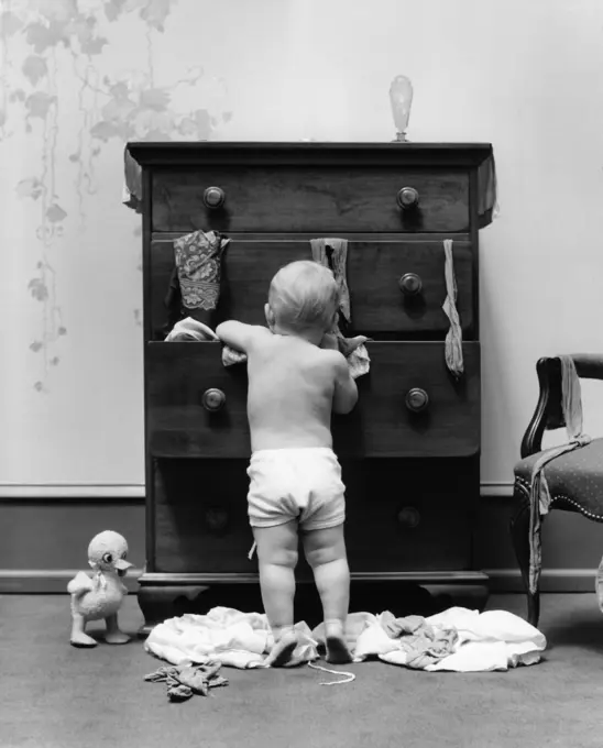 1940s TODDLER BABY PULLING CLOTHES OUT OF BUREAU DRAWERS MAKING A MESS