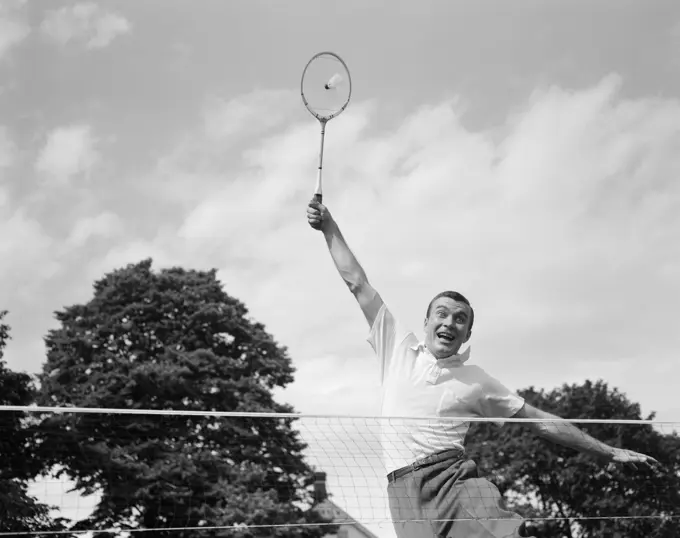 1950s 1960s MAN PLAYING BADMINTON JUMPING UP ARM EXTENDED RACQUET ABOUT TO HIT SHUTTLECOCK BIRDIE WACKY FUNNY EXTREME EFFORT LOB