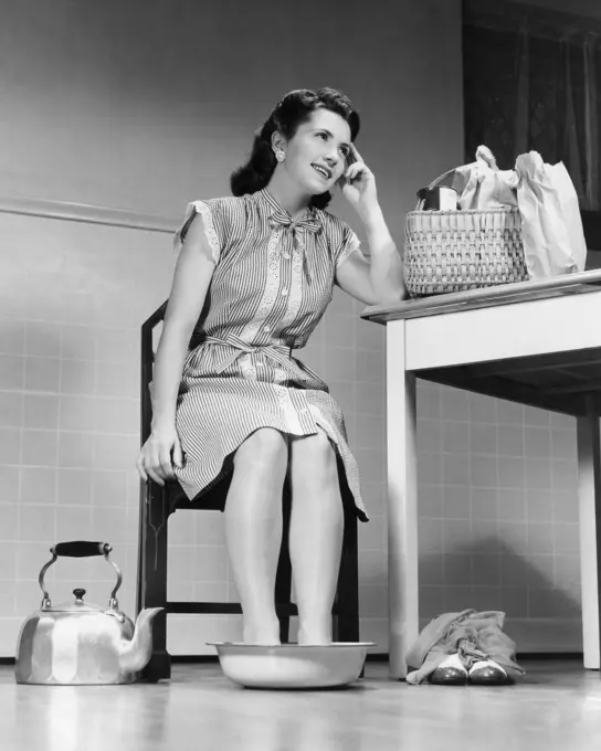 1940s HOUSE WIFE WOMAN HOME FROM GROCERY SHOPPING SHOES OFF SORE FEET SOAKING PAN OF HOT WATER