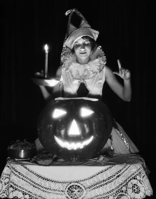 1920s 1930s WOMAN IN HARLEQUIN COSTUME HOLDING CANDLE LOOKING DOWN INTO CARVED PUMPKIN JACK-O-LANTERN 