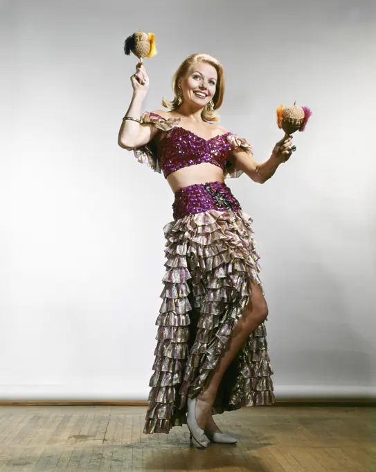 1960s FULL LENGTH BLONDE WOMAN CALYPSO CARIBBEAN COSTUME WITH BARE MIDRIFF SHAKING MARACAS LOOKING AT CAMERA