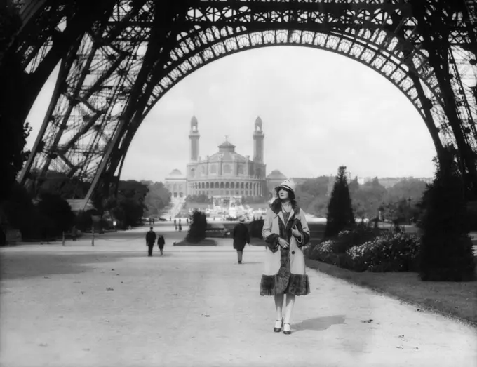 1920s WOMAN WALKING UNDER THE EIFFEL TOWER WITH THE TROCADERO IN BACKGROUND PARIS FRANCE 