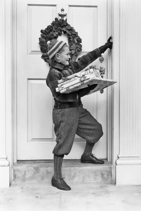 1930s 1940s BOY HOLDING WRAPPED PACKAGES RINGING BELL ON DOOR WITH CHRISTMAS WREATH 