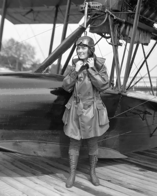 1920s FEMALE AVIATOR AVIATRIX LEATHER COAT CAP WITH GOGGLES AND LACE UP BOOTS PREPARING TO BOARD SEAPLANE