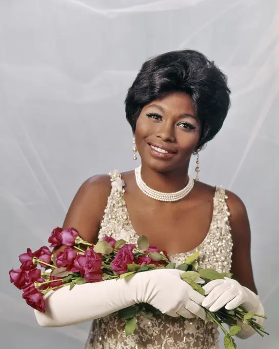 1960s AFRICAN-AMERICAN WOMAN IN PEARL BEADED DRESS WITH LONG WHITE GLOVES AND RED ROSES AWARD BEAUTY QUEEN