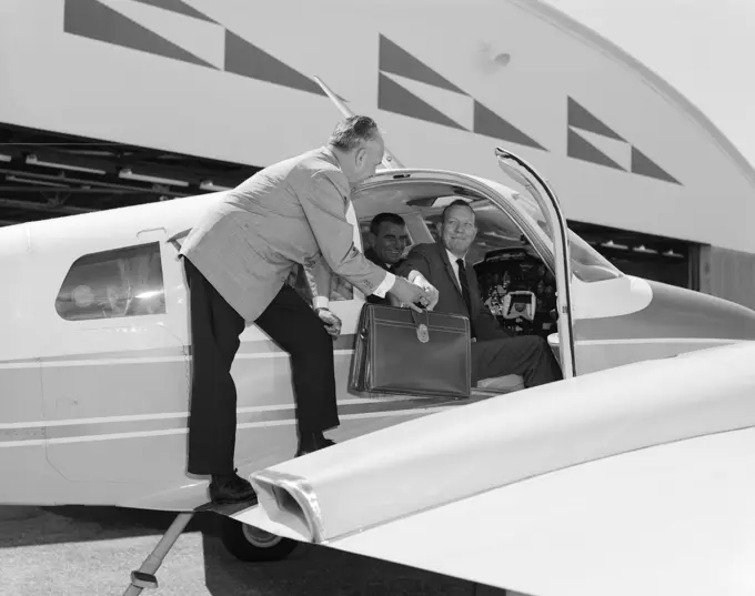 1960s SMILING BUSINESSMEN IN CESSNA 310G TWIN ENGINE AIRPLANE MAN HANDING LEATHER BRIEFCASE TO PASSENGER