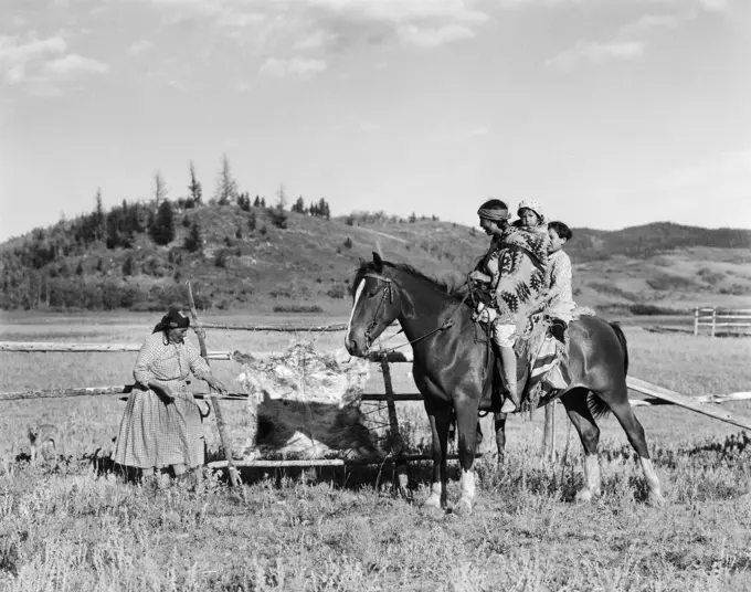 1920s THREE NATIVE AMERICAN CHILDREN ON HORSEBACK TALKING TO WOMAN TANNING HIDE STONEY SIOUX ALBERTA CANADA