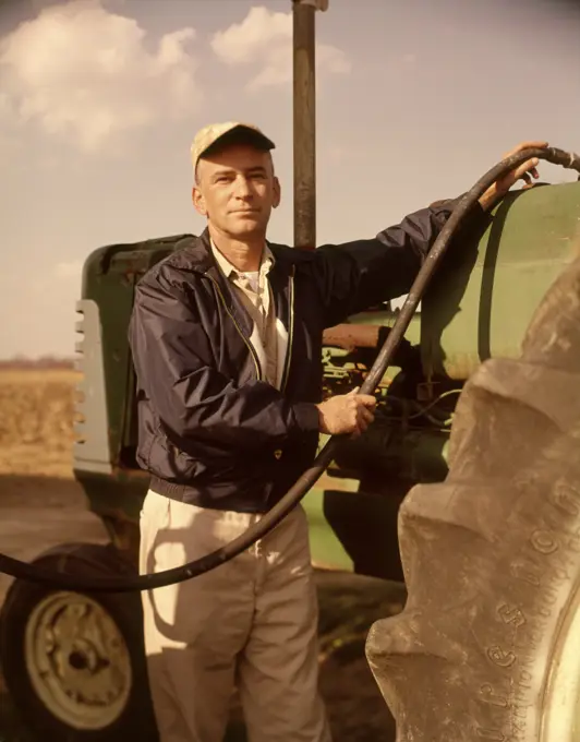 1960s PORTRAIT OF SERIOUS MAN FARMER LOOKING AT CAMERA FUEL INTO TRACTOR