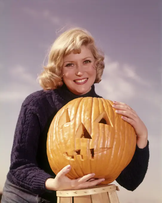 1960s SMILING BLOND WOMAN HOLDING JACK-O-LANTERN CARVED PUMPKIN LOOKING AT CAMERA