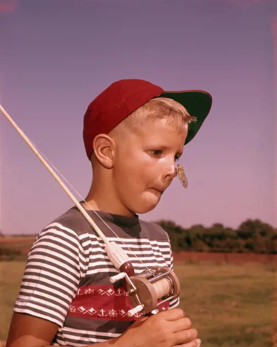 1950s SURPRISED BOY WITH CICADA INSECT ON HIS NOSE HOLDING FISHING POLE WEARING RED BALL CAP