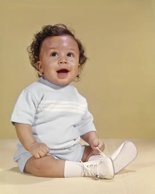 1970s SMILING CURLY HAIR AFRICAN AMERICAN BABY BOY SITTING HAPPY LOOKING UPWARD