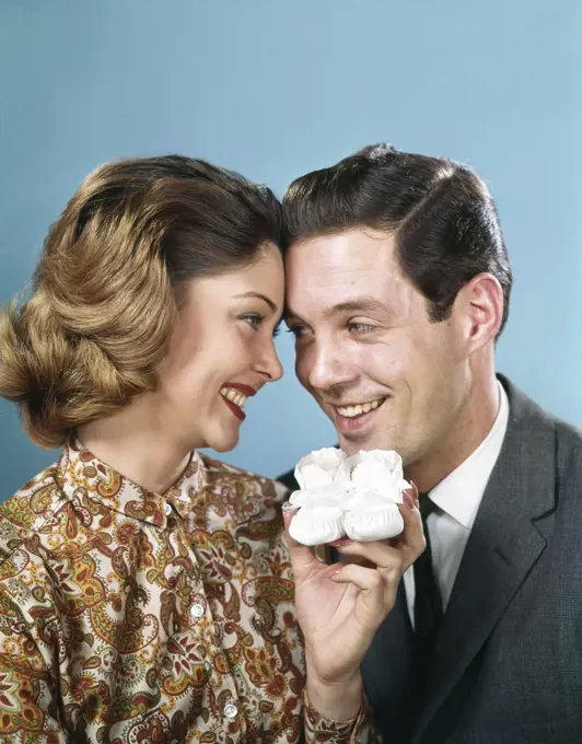 1960s SMILING COUPLE TOUCHING FOREHEADS LOOKING AT EACH OTHER HOLDING UP BABY SHOES 