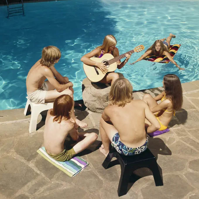 1970s 6 TEENS AROUND SWIMMING POOL LISTENING TO GIRL PLAYING GUITAR 