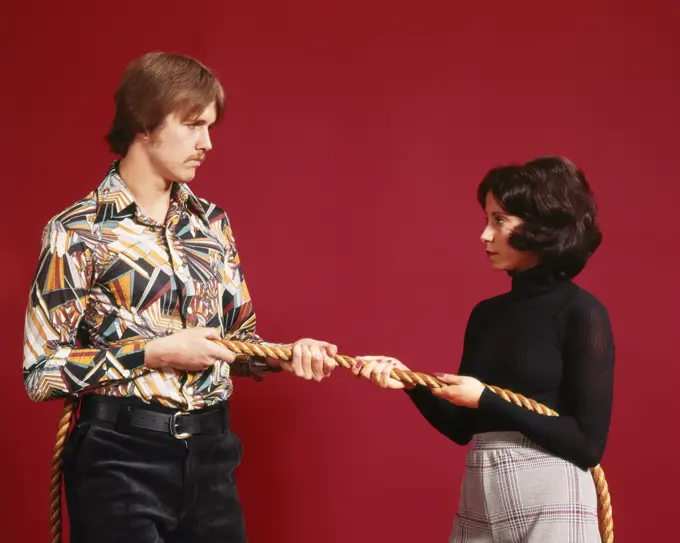 1970s ANGRY COUPLE AT OPPOSITE ENDS OF A ROPE TUG OF WAR 