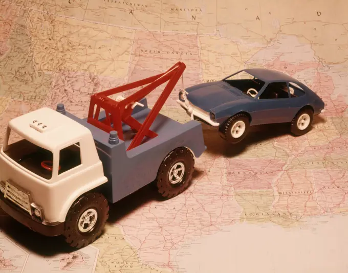 1970s TOY TOW TRUCK TOWING TOY CAR ACROSS PRINTED ROAD MAP BACKGROUND SYMBOLIC AUTOMOBILE ROAD SERVICE REPAIR