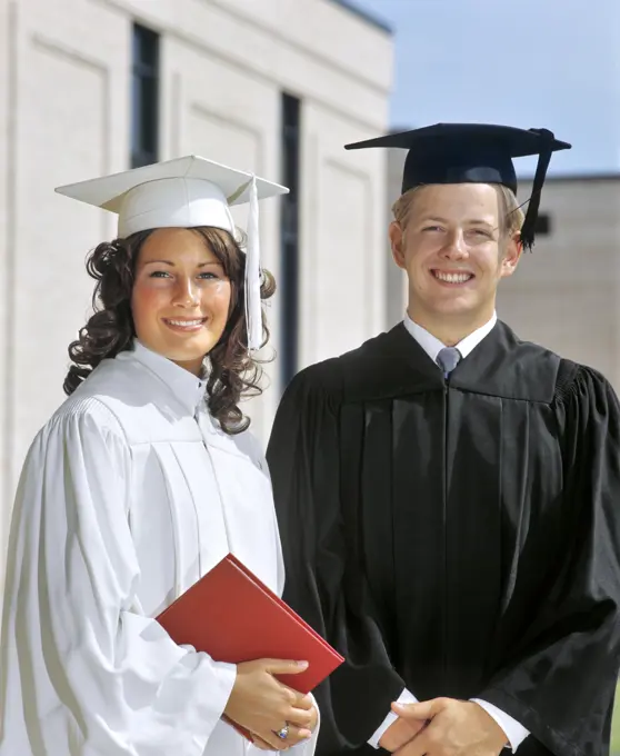 1970s PORTRAIT STUDENT COUPLE IN GRADUATION ROBES LOOKING AT CAMERA 