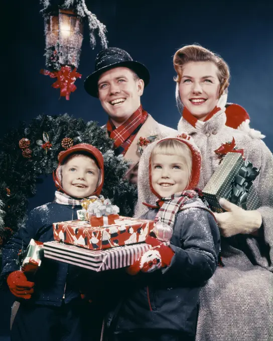 1950s FAMILY MAN WOMAN TWO KIDS HOLDING CHRISTMAS PRESENTS SMILING STANDING BENEATH LANTERN