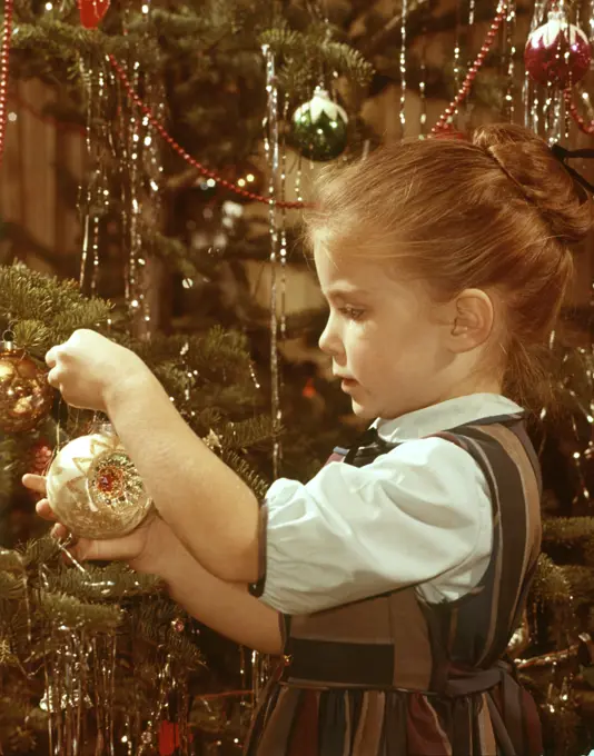 1960s PROFILE SERIOUS LITTLE GIRL HANGING GLASS ORNAMENT ON CHRISTMAS TREE BRANCH