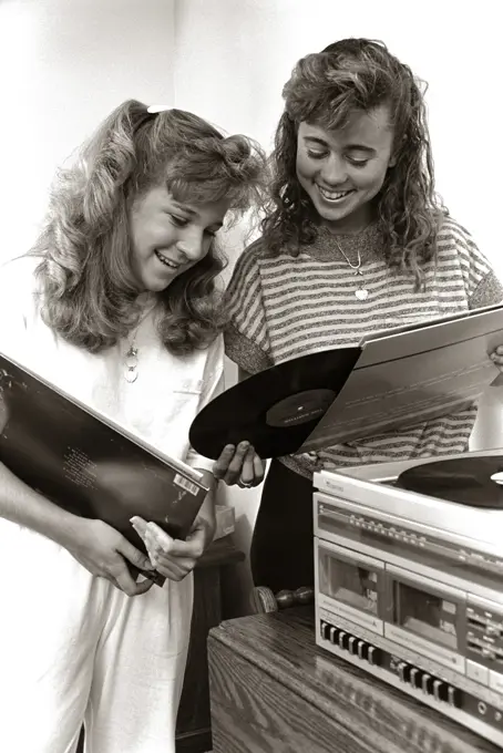 1980s 2 TEENAGE GIRLS READING VINYL RECORD ALBUM JACKET COVERS LISTENING TO LONG PLAYING PHONOGRAPH PLAYER