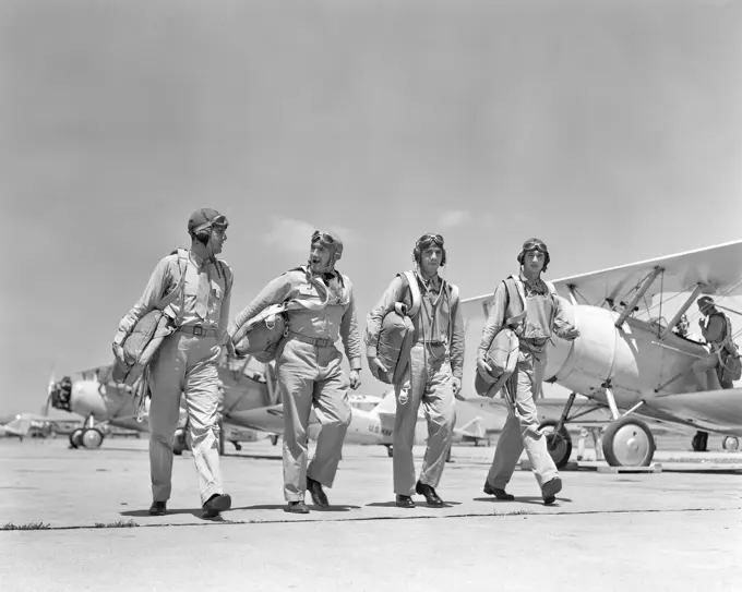 1940S FOUR U.S. NAVY PILOTS WALKING TOGETHER ON TARMAC RETURNING FROM AIR MANEUVERS AT THE PHILADELPHIA NAVY YARD PA USA