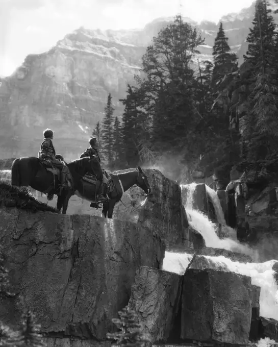 1920s 1930s COUPLE MAN WOMAN ON HORSES BY WATERFALL IN PINE FOREST GIANTS STEPS PARADISE VALLEY ALBERTA CANADA