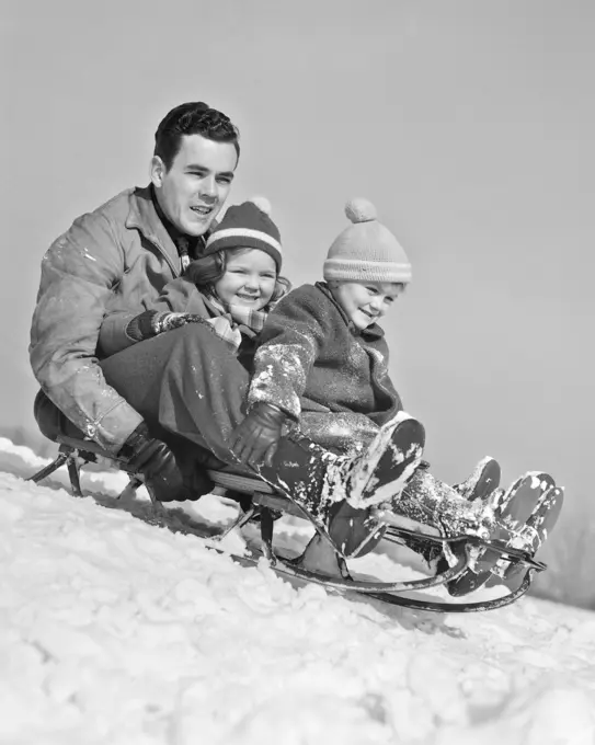 1930s 1940s FATHER TWO CHILDREN ON SLED IN SNOW GOING DOWN HILL