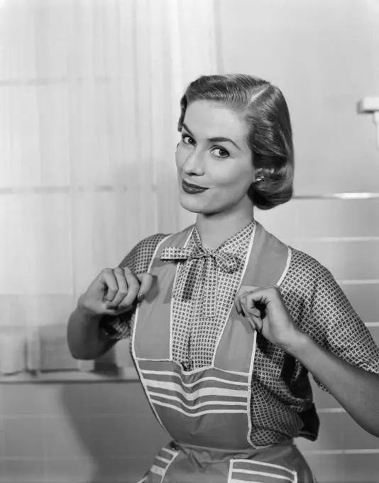 1950S Housewife Wearing Apron With Thumbs Proudly Hooked On Straps