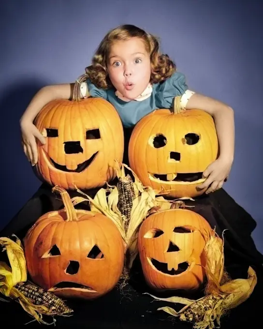 1950s LITTLE GIRL STANDING ABOVE FOUR CARVED HALLOWEEN PUMPKINS JACK-O-LANTERNS WITH SCARED FACIAL EXPRESSION LOOKING AT CAMERA