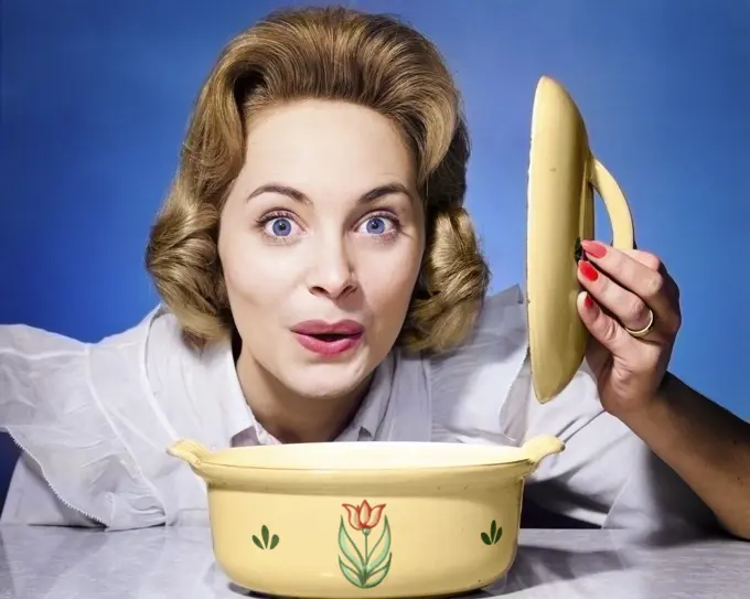 1960s 1950s SURPRISED HAPPY WOMAN HOUSEWIFE COOK LIFTING THE LID OFF OF CASSEROLE DISH LOOKING AT CAMERA