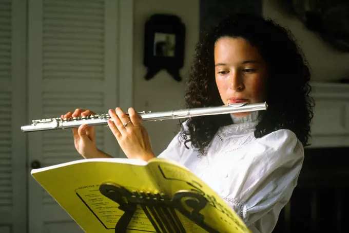 1980s BRUNETTE TEENAGE GIRL PLAYING A FLUTE READING SHEET MUSIC ON BRASS MUSIC STAND