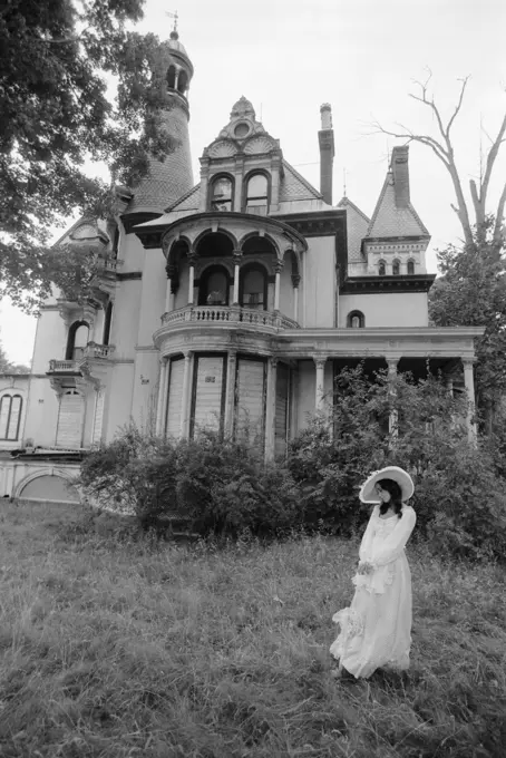 Woman In Victorian Costume Standing On Front Lawn Of Large Abandoned Haunted Victorian Home