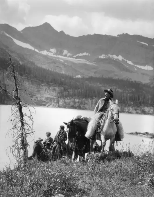 1920S 1930S Two Women One Man Riding Horses Western Saddles Cowboy Wearing Wool Chaps By Mountain Lake In Canada