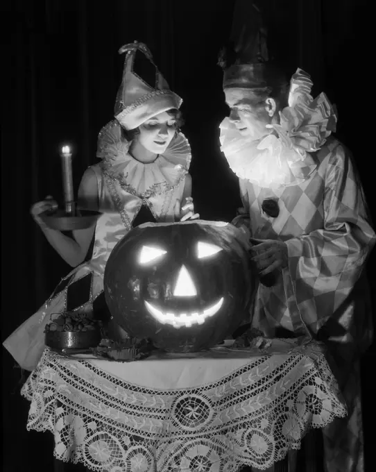 1920S 1930S Couple In Costumes Looking Down Into Candle Light From Carved Pumpkin Jack-O-Lantern