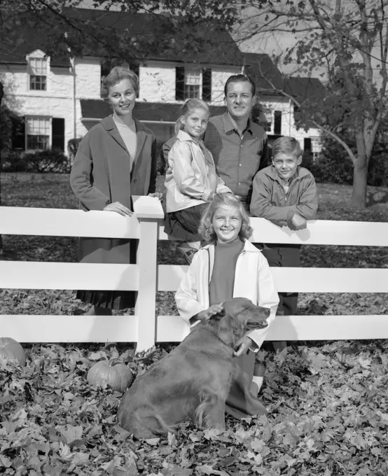 1960S Family Portrait Father Mother Two Daughters Son And Dog Gathered Around White Front Yard Fence Looking At Camera