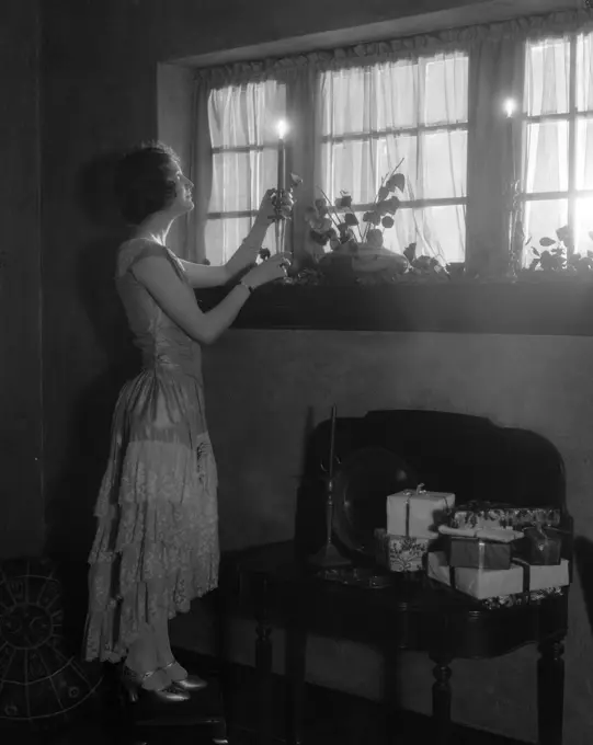 1920S Woman Party Dress Ruffles On Skirt Placing A Lighted Candle In Window Gifts Presents Wrapped On Side